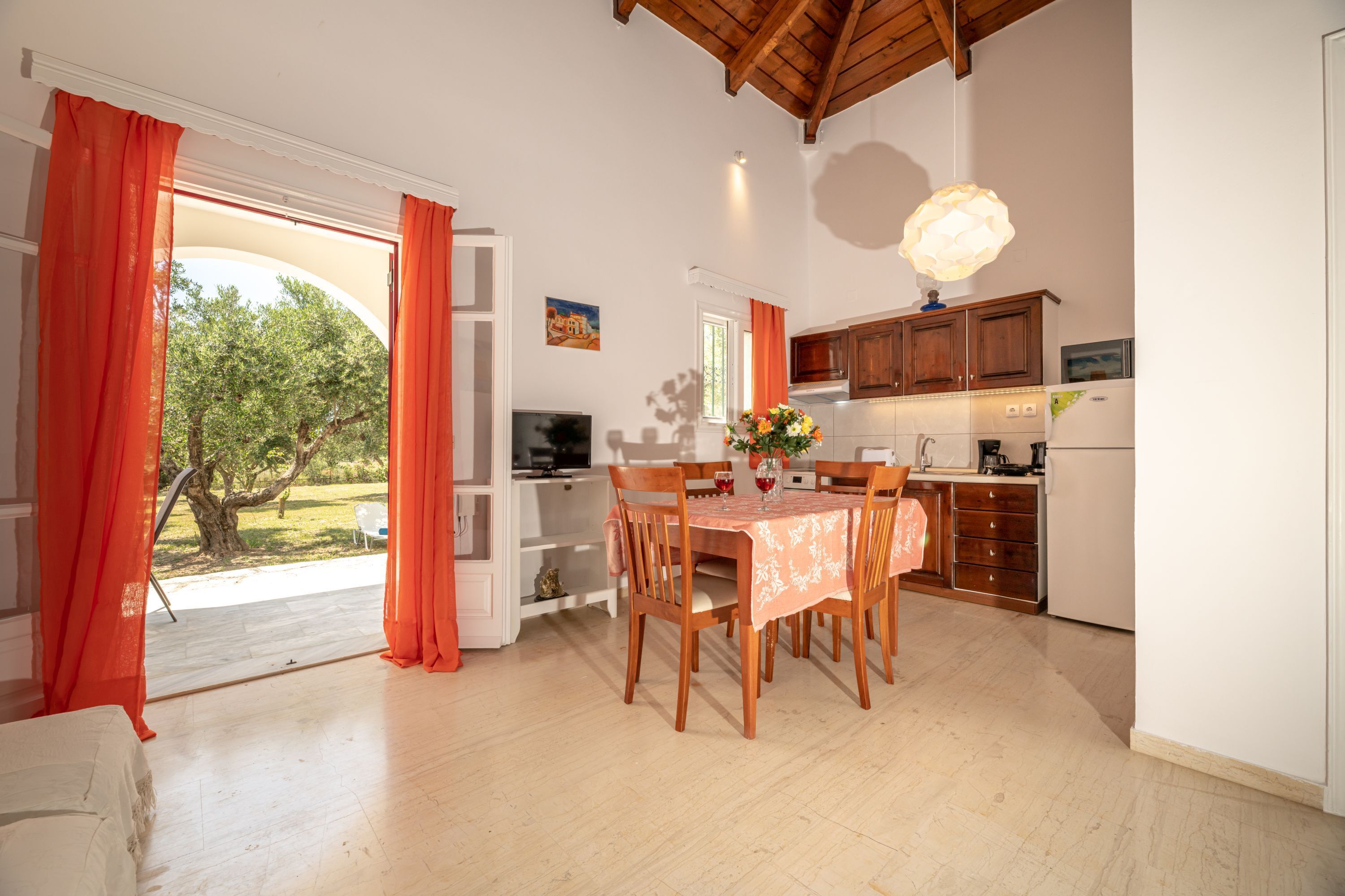 A spacious dining area with a table set for four, a kitchen with wooden cabinets, and a large window with curtains.