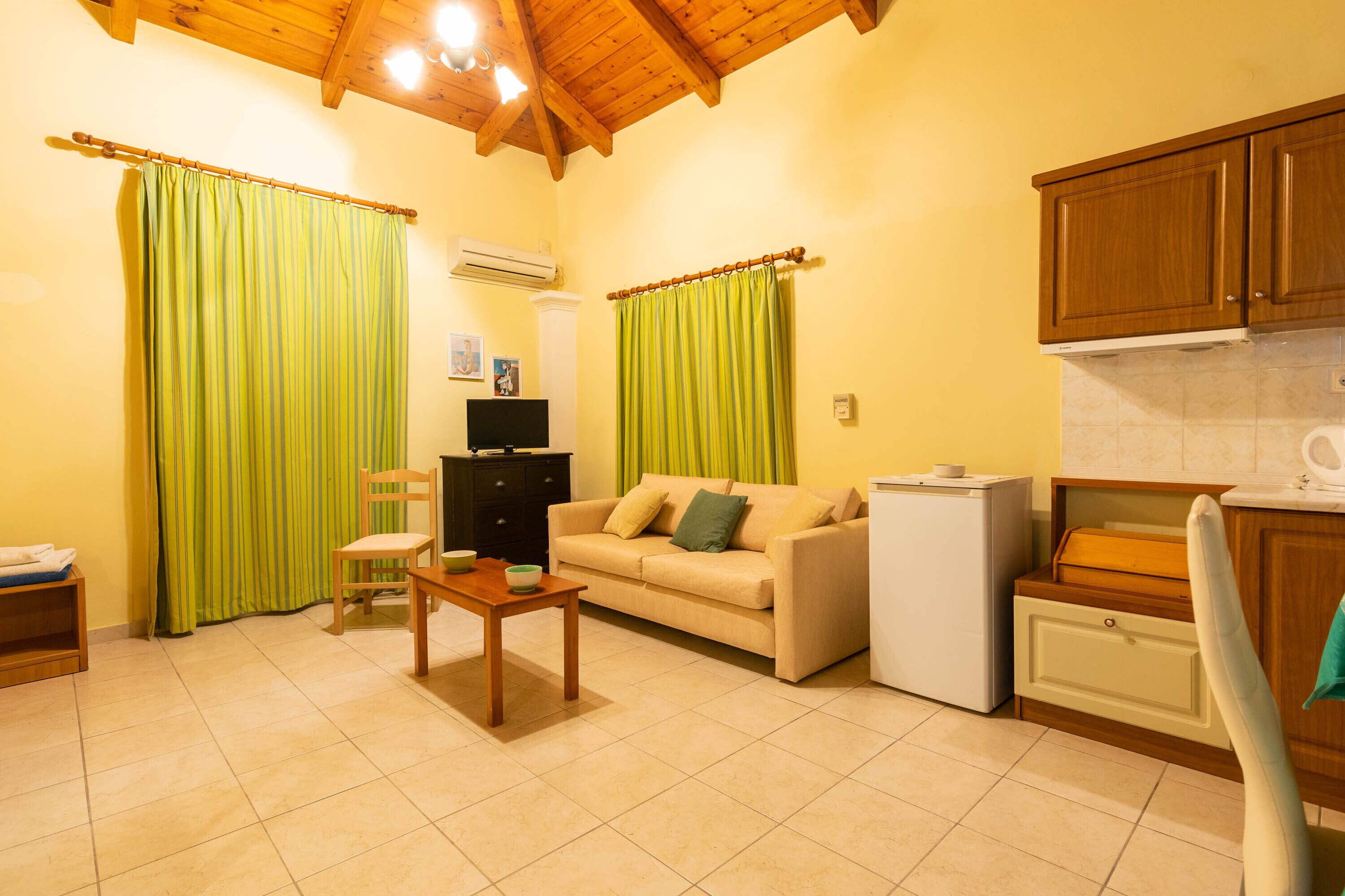 A compact living space with a sofa, a small table, a TV, and a kitchen area with cabinets and a refrigerator.