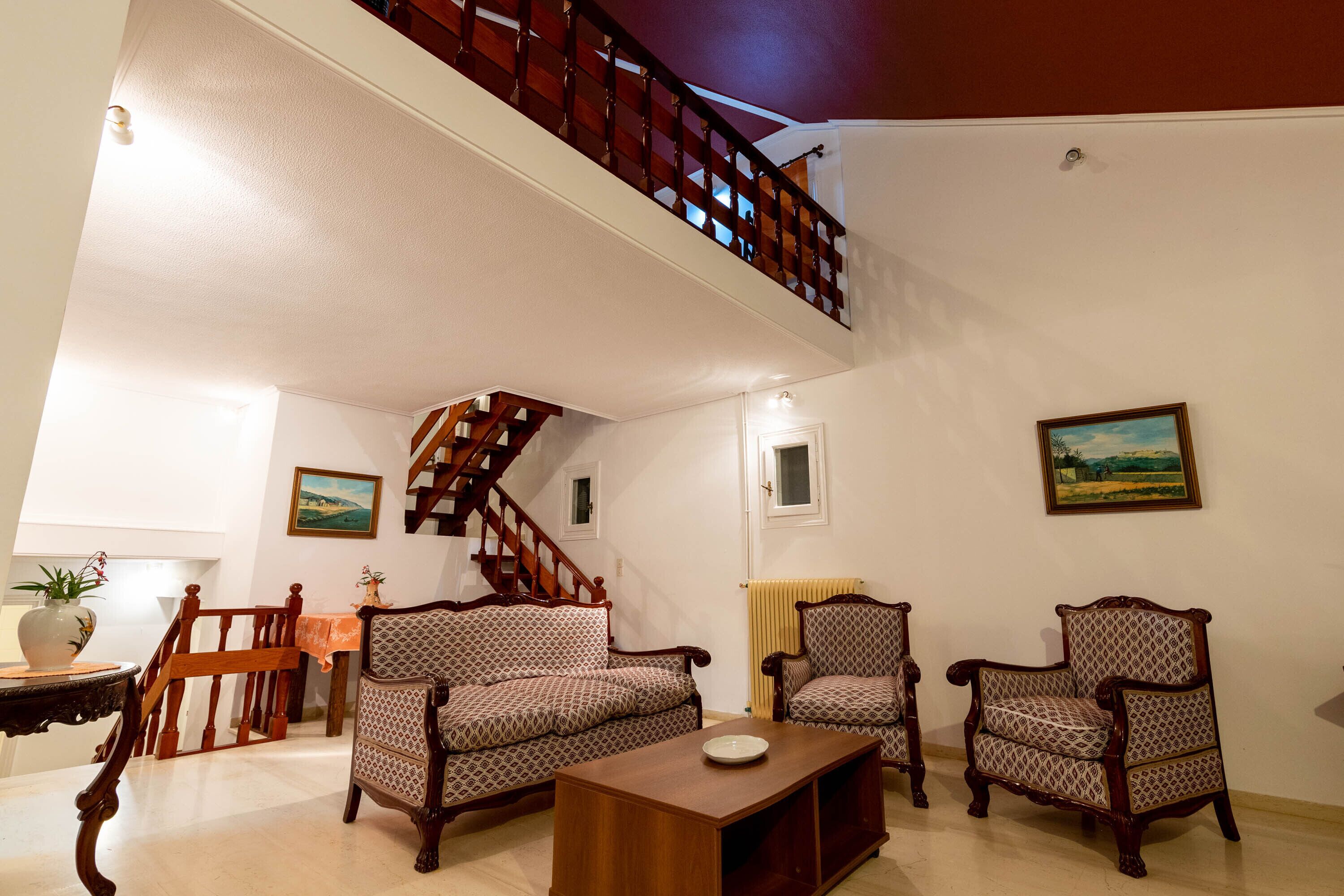 A spacious living room with a wooden staircase, two patterned armchairs, a sofa, and a coffee table.