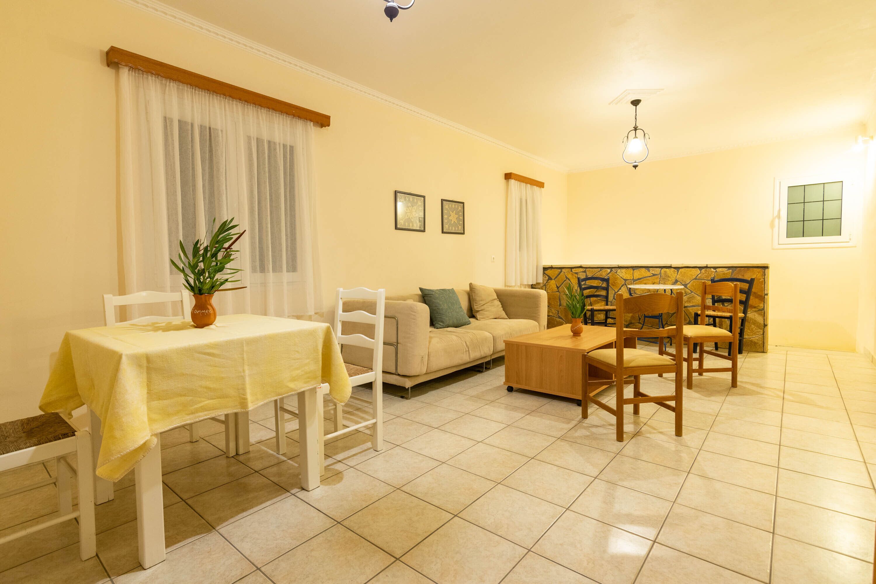 A living room with a sofa, a dining table with chairs, a coffee table, and a potted plant.