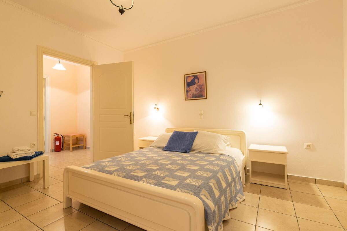 Ein Schlafzimmer mit einem Bett, Nachttischen, einer Bank und einer Tür zu einem anderen Raum.