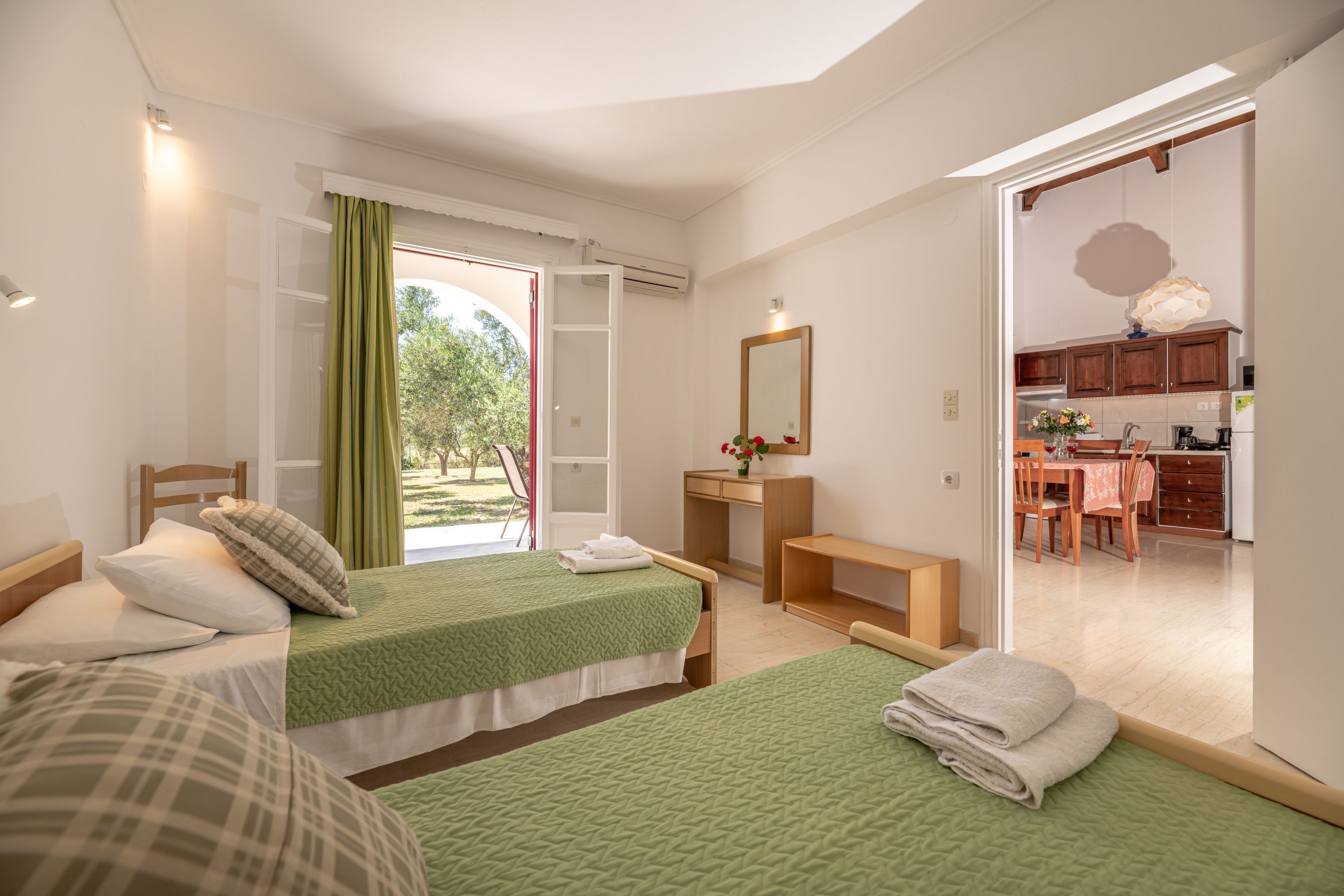 A bedroom with two beds, a desk, and a view of the garden.