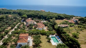 Vista aérea de uma propriedade costeira com várias casas, piscina e vista ampla para o mar.