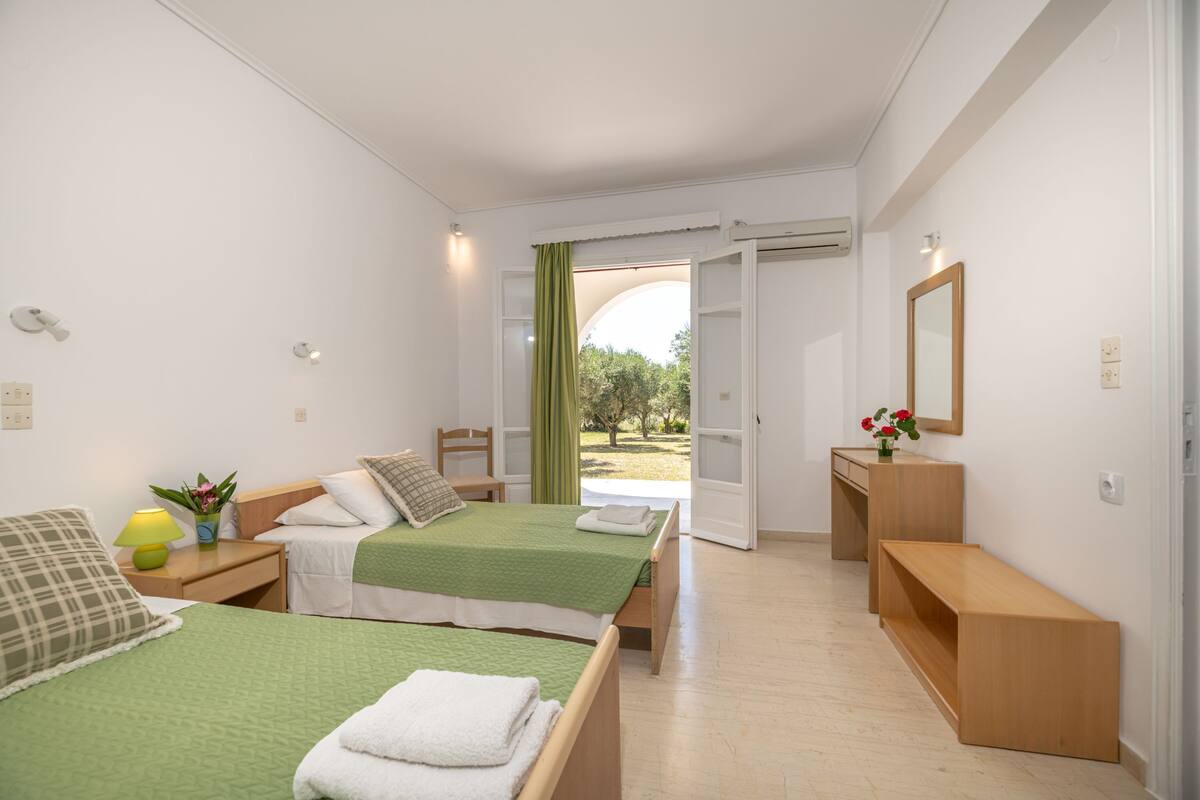 Ein Hotelzimmer mit zwei Betten, einem Schreibtisch, einem Stuhl und Blick ins Freie.