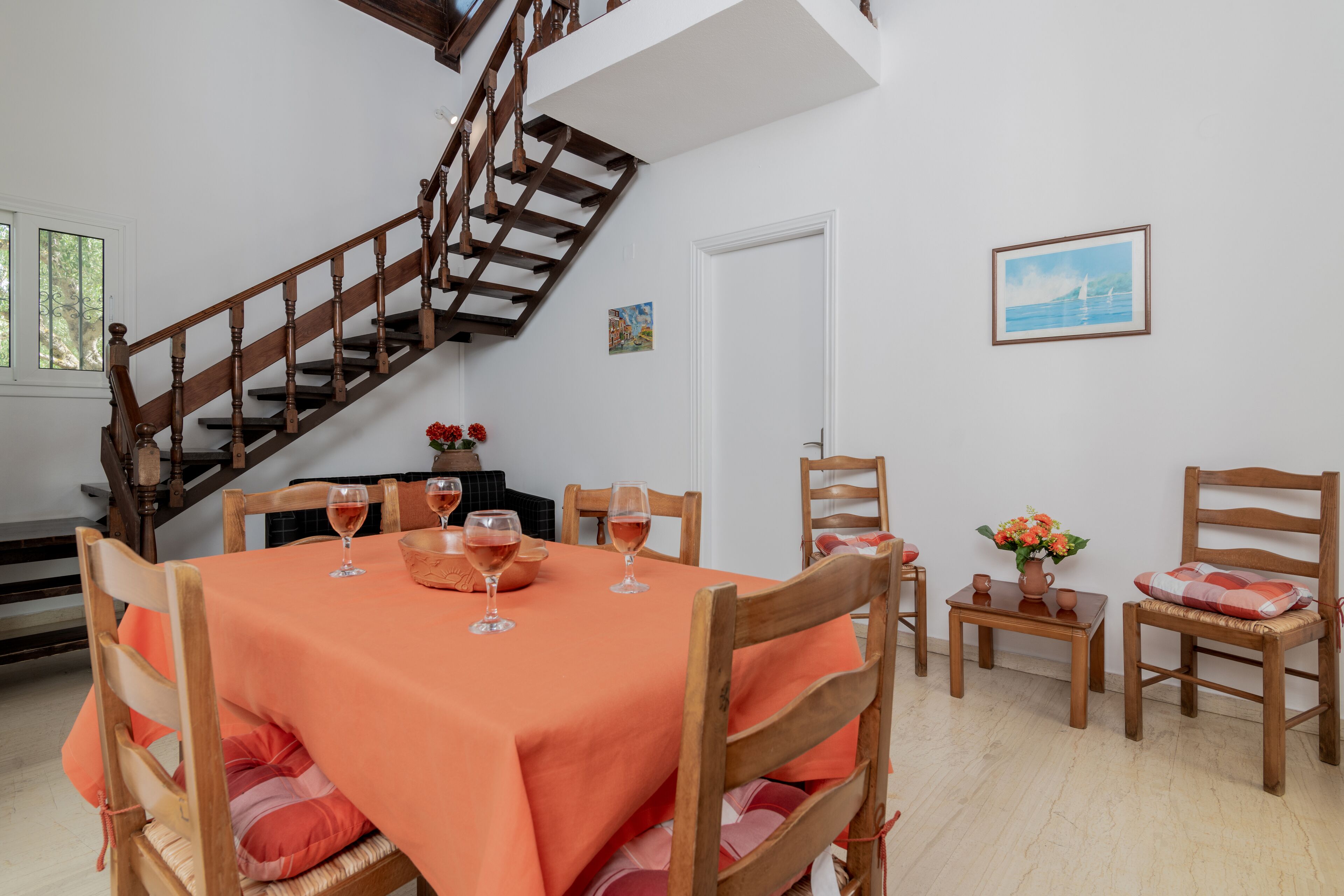 Uma sala de jantar com escada de madeira, mesa posta com copos de vinho e cadeiras com almofadas.