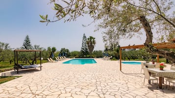Relax by the serene pool surrounded by lush greenery and a shaded pergola.