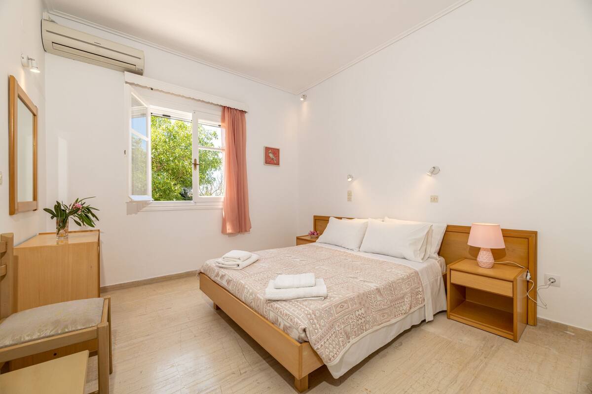Ein Schlafzimmer mit Bett, Nachttisch, Lampe und einem Fenster mit Vorhängen.