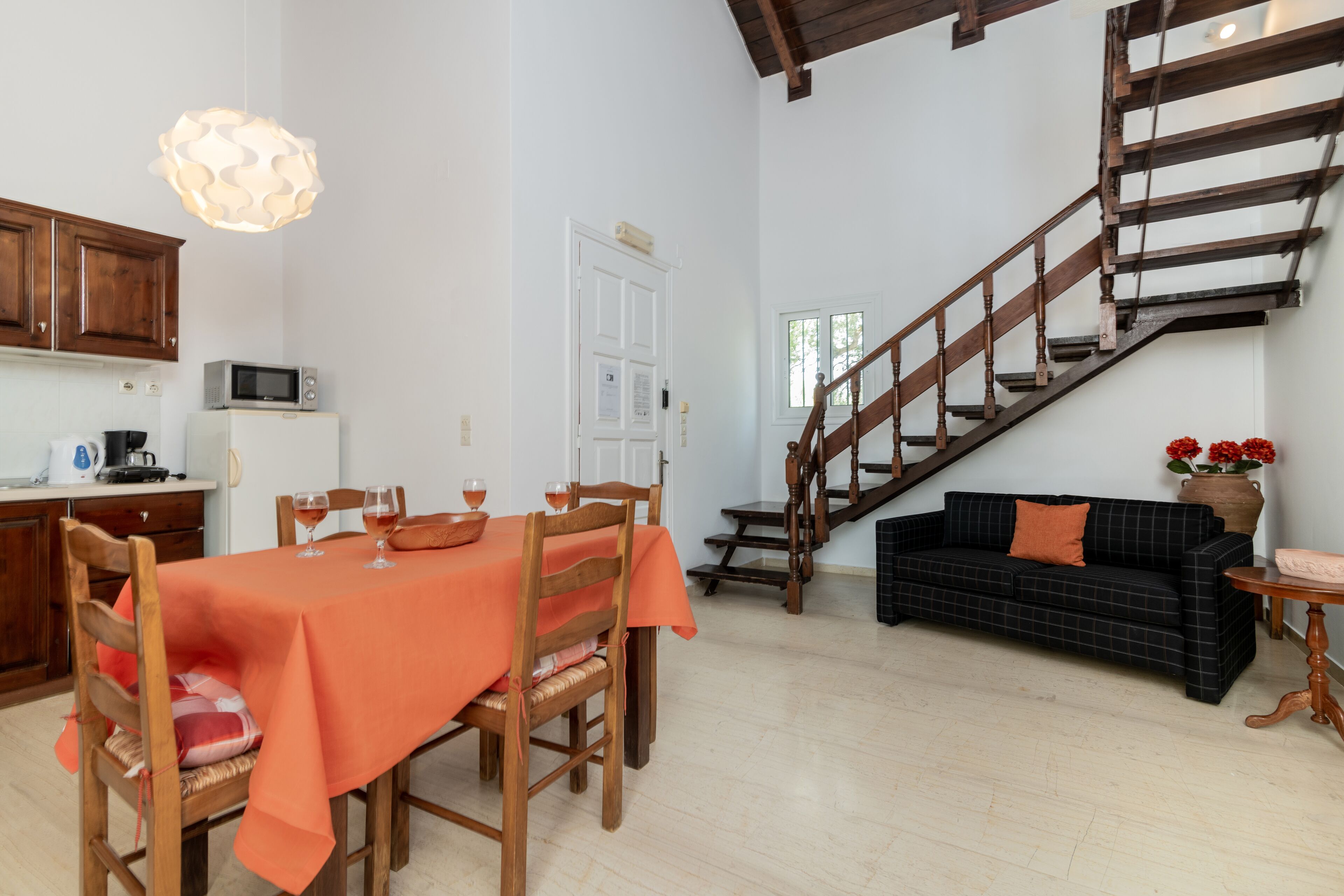 A dining area with a table set for four, a kitchen with a microwave, and a staircase leading to an upper level.