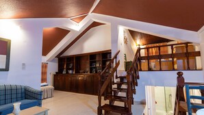 Ampla sala de estar com escada de madeira, um sofá azul e uma área de cozinha com armários de madeira.
