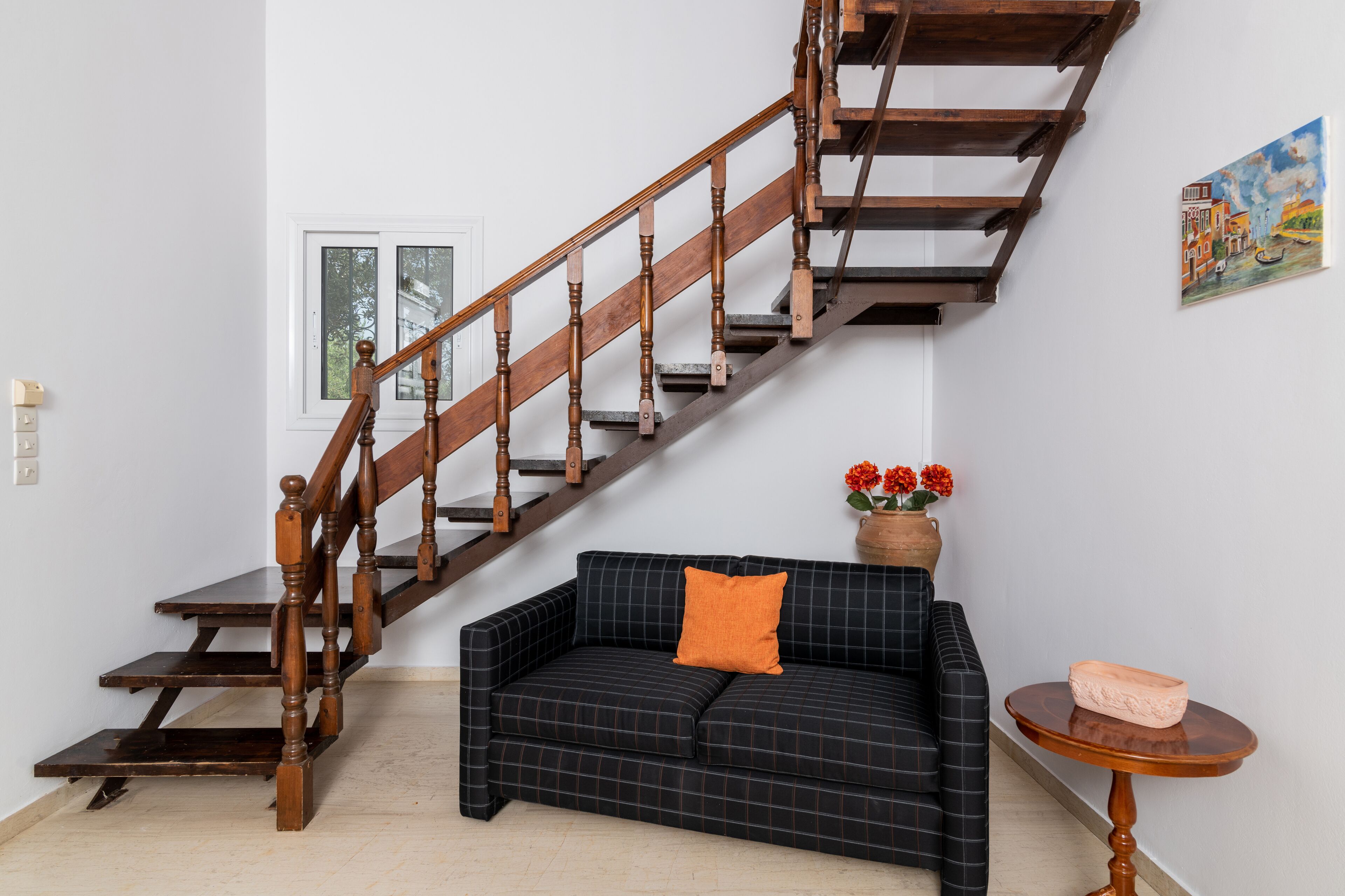 A staircase with wooden balusters and a dark checkered sofa with an orange pillow.