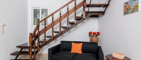 A staircase with wooden balusters and a dark checkered sofa with an orange pillow.