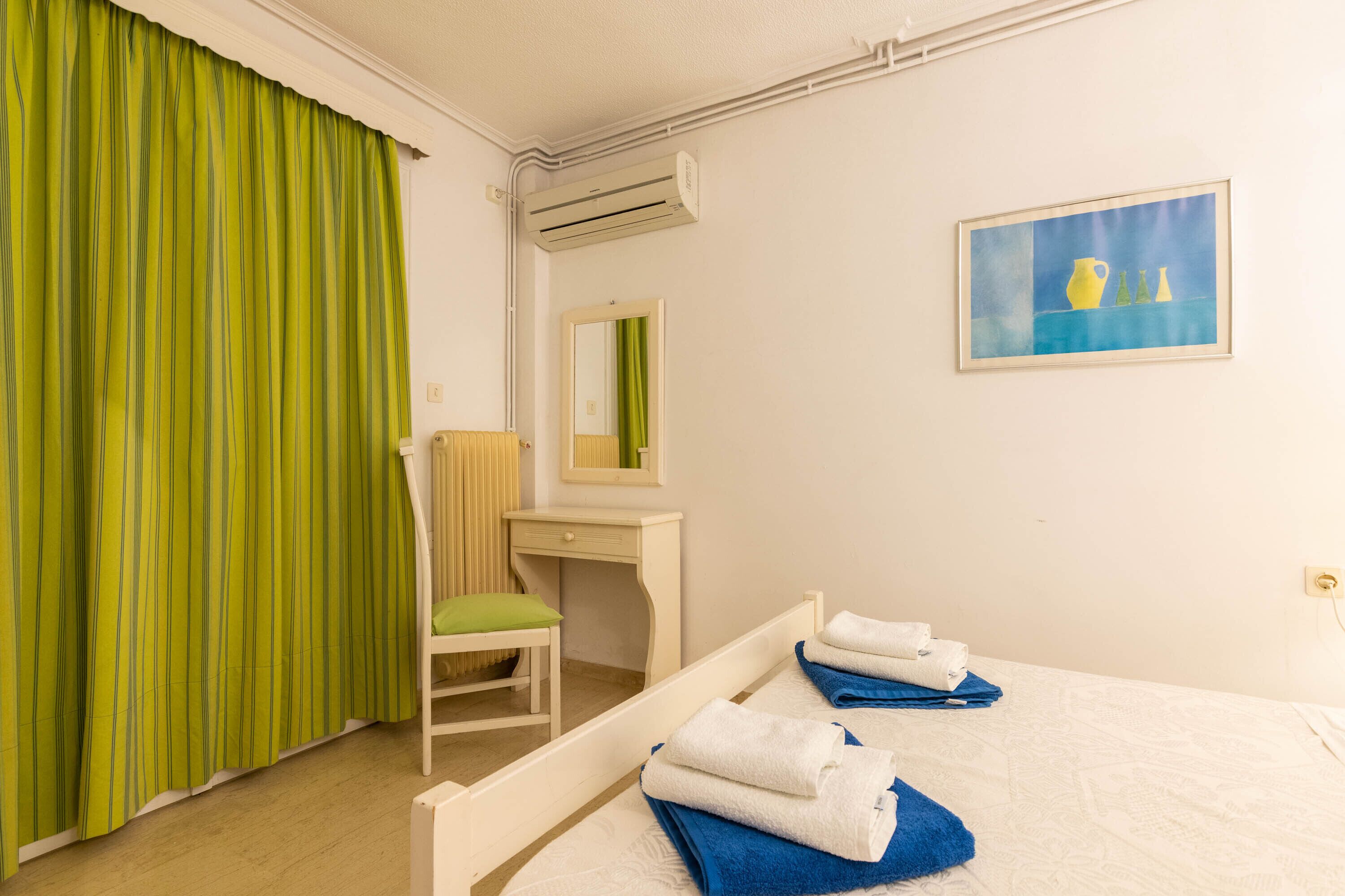 A hotel room with a bed, a desk, a chair, and a painting on the wall.