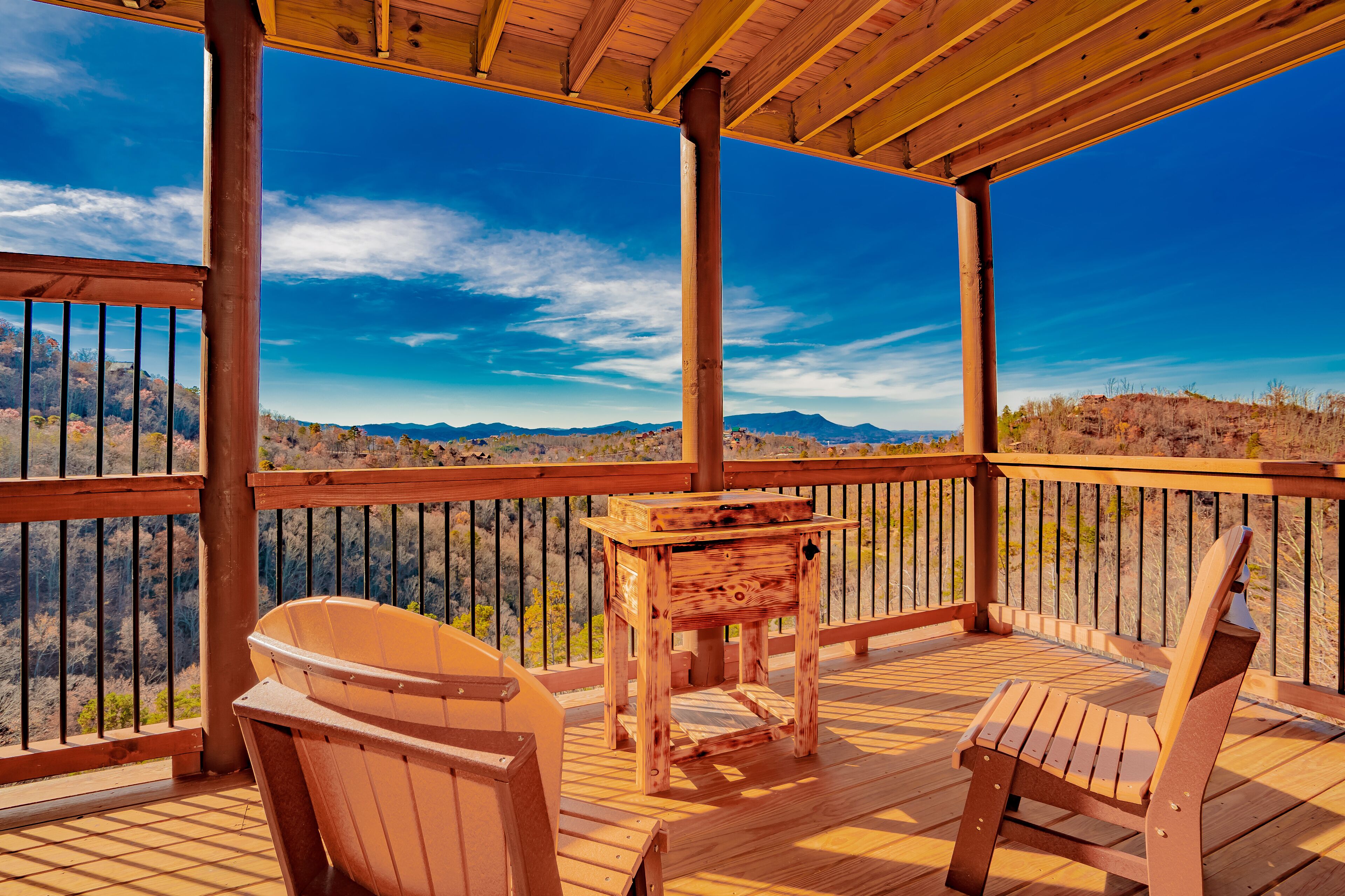 A wooden deck with a wooden table and chairs, overlooking a mountainous landscape.