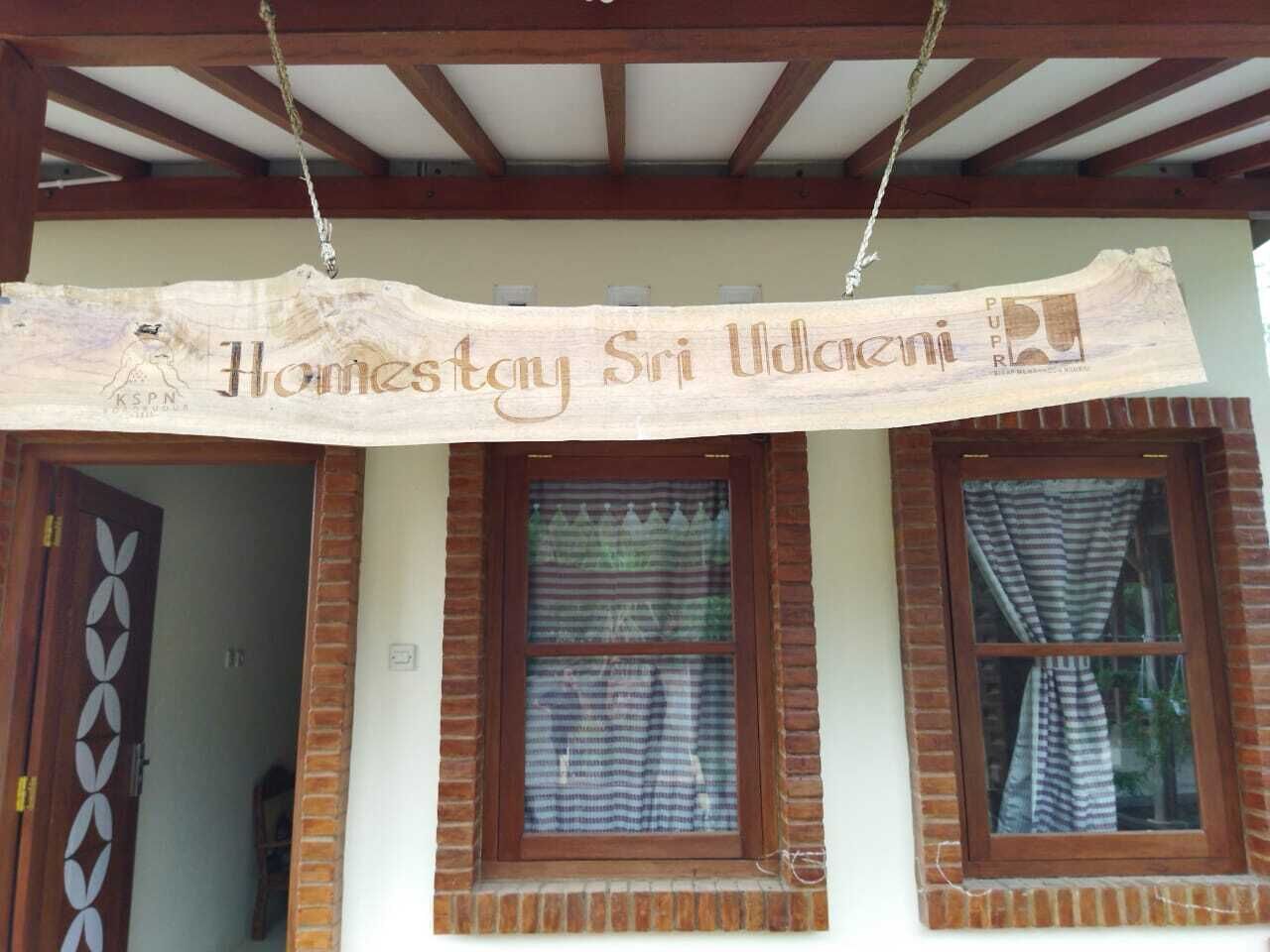 Un edificio con un cartel que dice "Homestay Sri Udaiani" y una puerta de madera con un diseño geométrico.