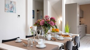 A dining area with a table set for two, a vase of flowers, a pitcher, and a fruit bowl. - Villa Levante (Lido di Camaiore)