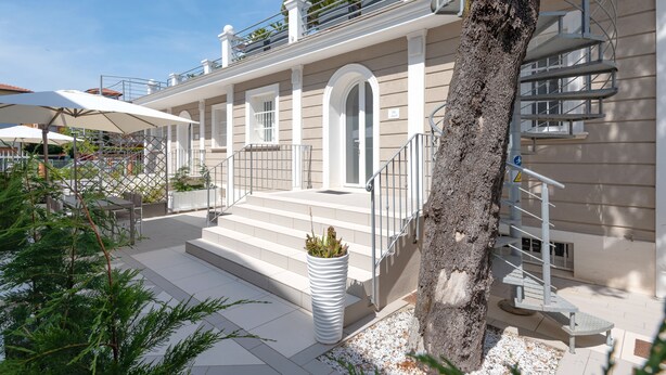 A modern building with a staircase leading to a balcony, outdoor seating area, and a large planter with plants. - Villa Levante (Lido di Camaiore)
