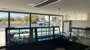 A modern interior with large windows, a glass display case with food items, and a kitchen area. - GRAND ÖZALP AİRPORT HOTEL (Ortaca)
