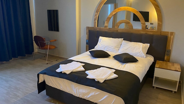 A neatly made bed with white and black bedding, a wooden headboard, and a bedside table with a lamp. - GRAND ÖZALP AİRPORT HOTEL (Ortaca)