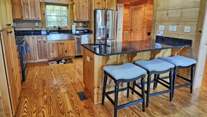 A wooden cabin kitchen with a central island, bar stools, and a refrigerator. - Escape to Daltons Creek Cabin in Creston, NC, perfect for family fun! (Creston)