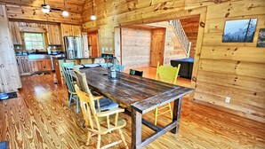 A wooden interior with a central dining table, chairs, a kitchen area, and a staircase. - Escape to Daltons Creek Cabin in Creston, NC, perfect for family fun! (Creston)