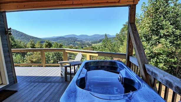 Een hottub op een houten terras, met uitzicht op bergen en bomen.
