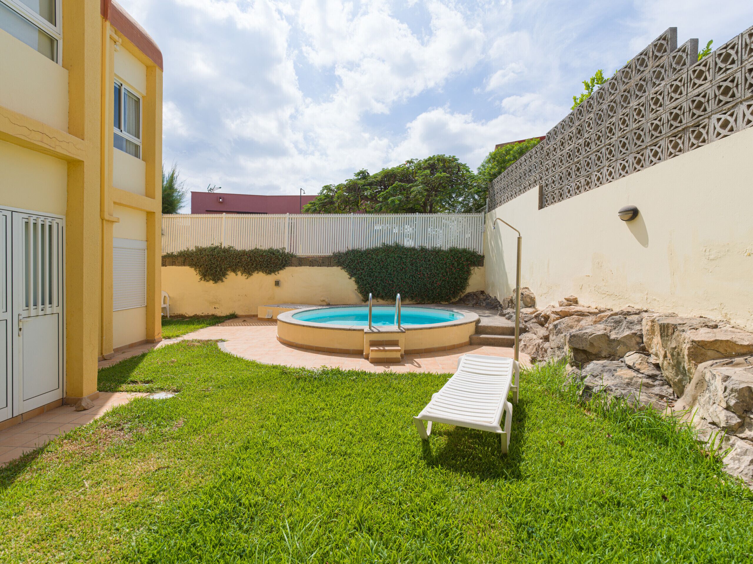 A backyard with a swimming pool, a lounge chair, and a small garden area.