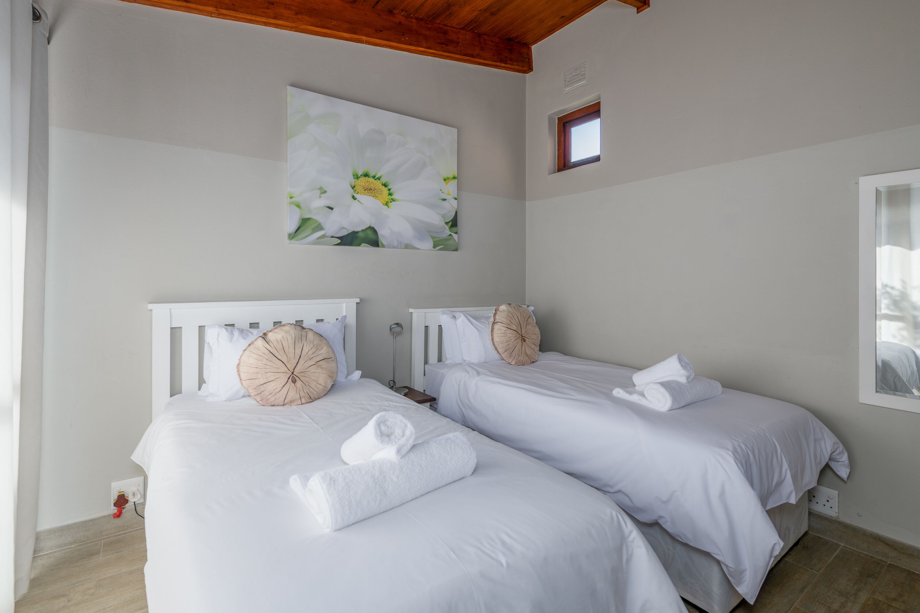 Habitació d'hotel amb dos llits, roba de llit blanca i un quadre de flors blanques a la paret.
