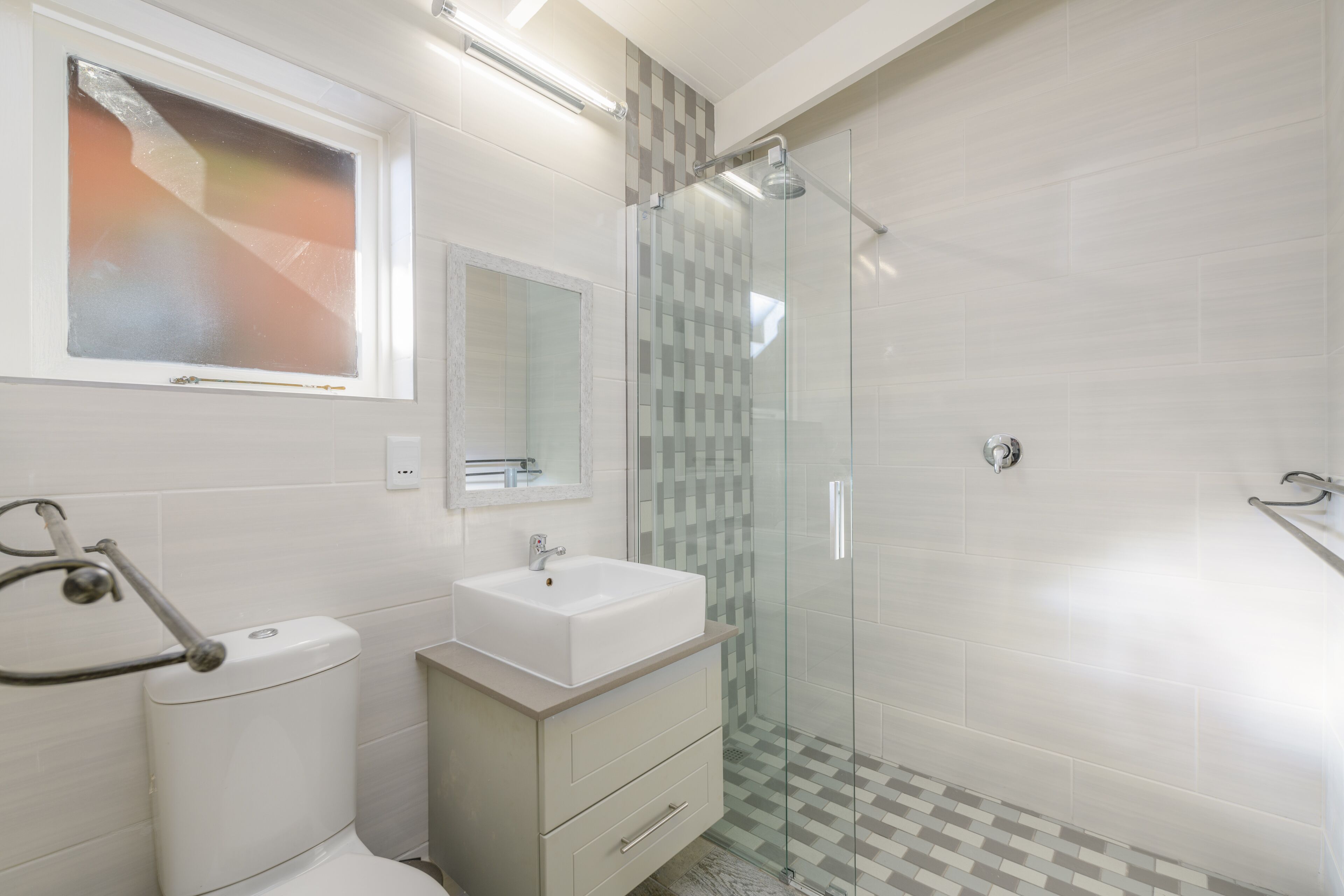 Een moderne badkamer met een douchecabine van glas, een witte wastafel en een toilet met een greep.