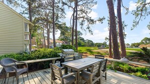 A wooden deck with a table and chairs, surrounded by greenery and trees.
