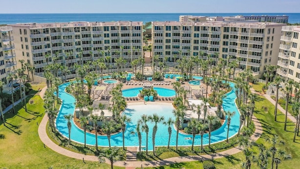 Un hotel con piscina central rodeada de palmeras y múltiples balcones.