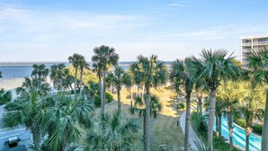 Un hotel frente a la playa con palmeras, piscina y vista al océano.