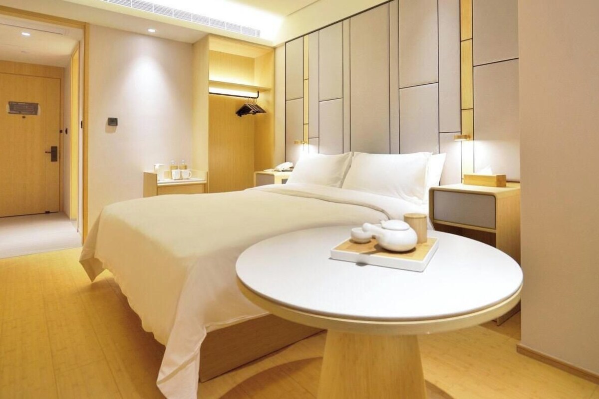 A hotel room with a large bed, bedside table, and a small round table with a teapot and cups.