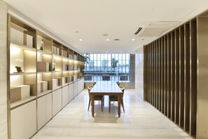 A modern interior with a long table and chairs, a built-in shelving unit, and a view through large windows. - Ji Hotel (Shanghai)