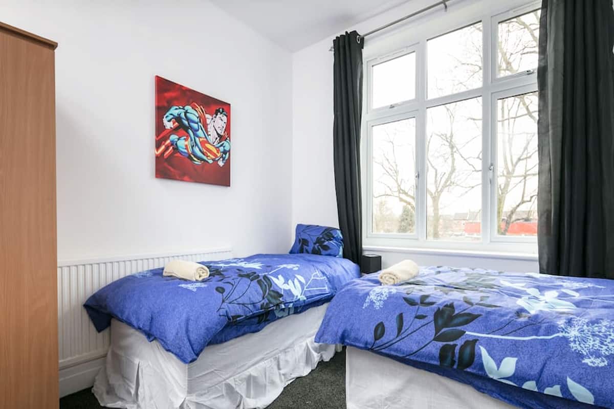 A bedroom with two beds, a radiator, a window with curtains, and a painting on the wall.