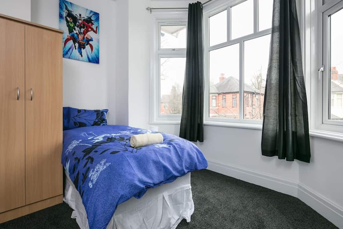 A bedroom with a bed, a wardrobe, a window with curtains, and a painting on the wall.