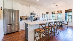 A spacious kitchen with white cabinets, stainless steel appliances, and a large island with bar stools. - Golf Carts ~ Patio ~ Balcony ~ Community Pool (Miramar Beach)