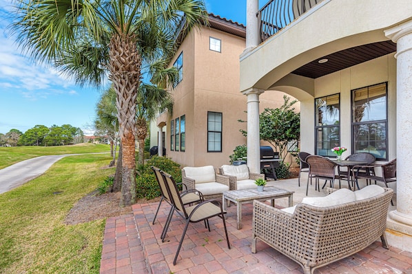 A patio area with wicker furniture, a palm tree, and a view of a road.