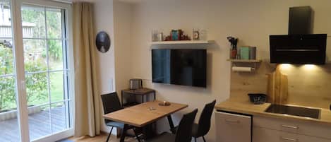 A modern kitchen with a wooden table, black chairs, a built-in oven, and a TV mounted above the counter.