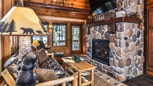 L’intérieur d’un chalet accueillant, avec une cheminée en pierre, un plafond en bois et un canapé agrémenté d’un lampadaire sur le thème de l’ours.