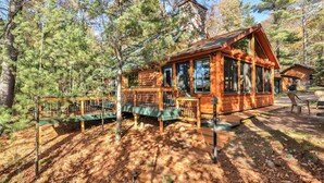 Une cabane en rondins dotée d’une terrasse, entourée d’arbres.
