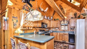 L’intérieur d’un chalet rustique, avec des murs en bois, un îlot central doté de sièges, un coin cuisine équipé d’appareils électroménagers et des bois de cerf décoratifs.