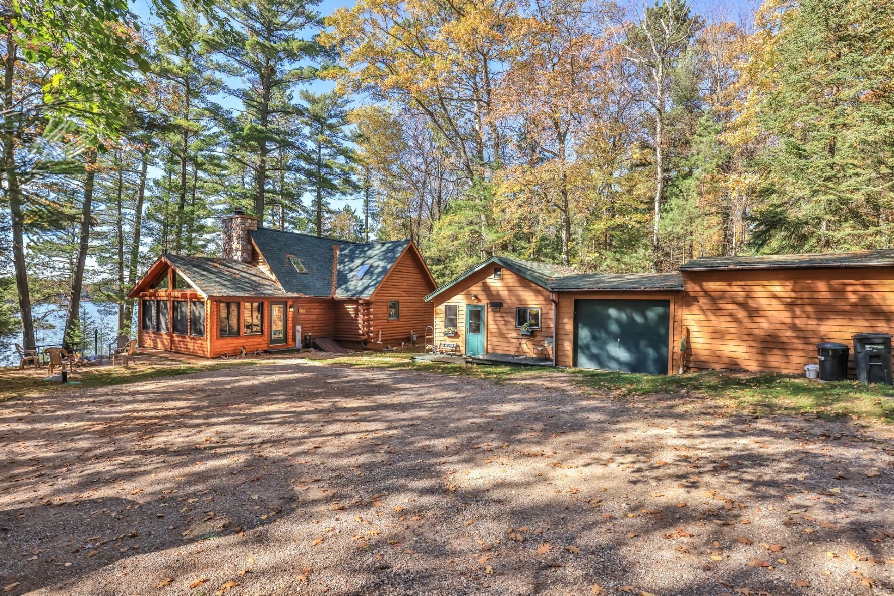 A cabin with a large garage, a covered porch, and a view of the surrounding forest.