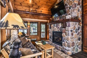 L’intérieur chaleureux d’un chalet avec une cheminée en pierre, un plafond en bois et un canapé agrémenté d’un lampadaire sur le thème de l’ours.