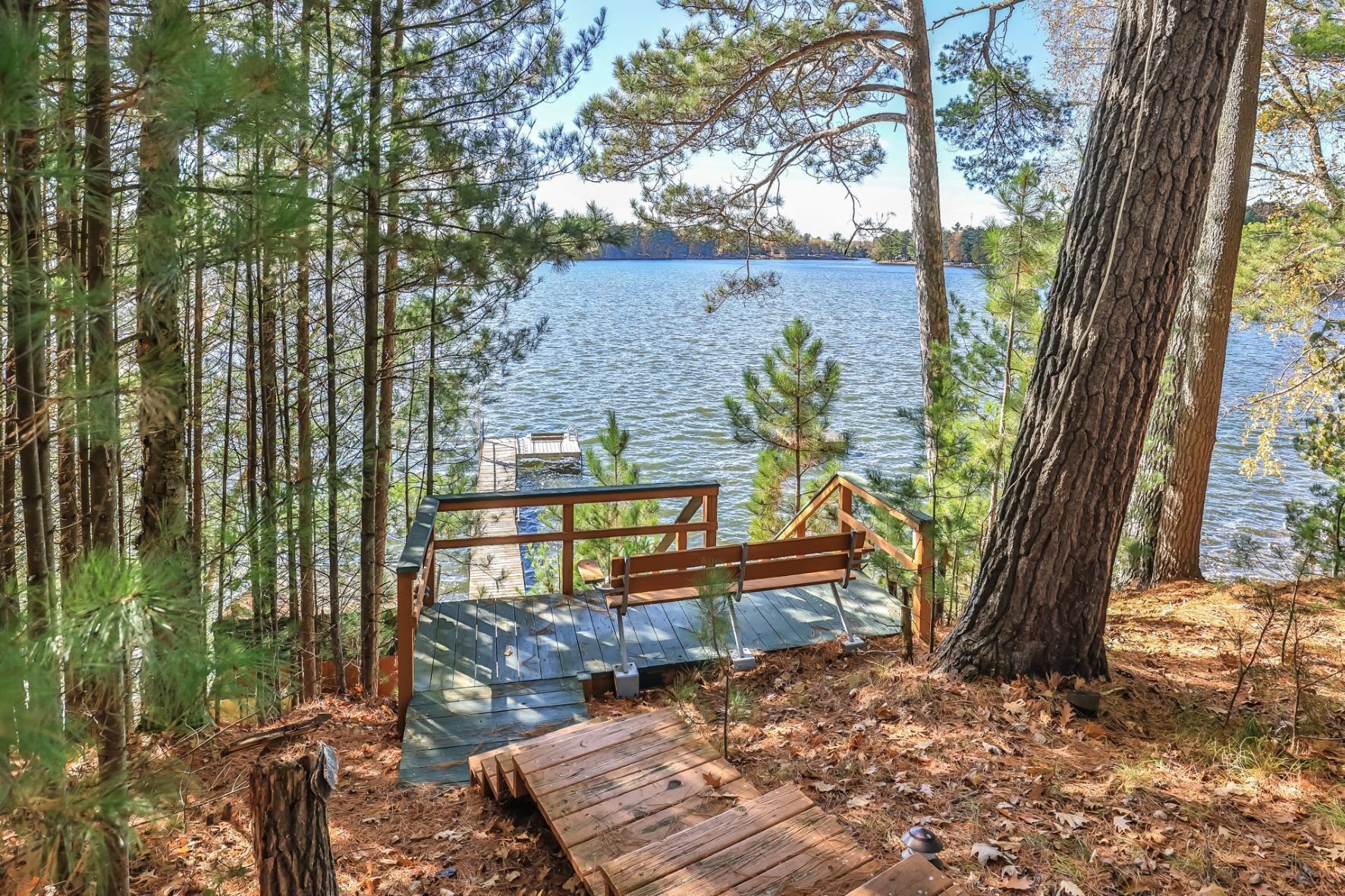 Una terraza de madera con un banco que da a un lago, rodeado de árboles.
