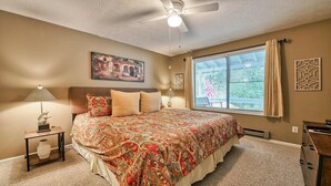 Una camera da letto con un letto grande, una ventola a soffitto, un quadro e una finestra con tende.