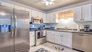Una cucina moderna con elettrodomestici in acciaio inossidabile, mobili bianchi, forno a microonde integrato e illuminazione a sospensione.