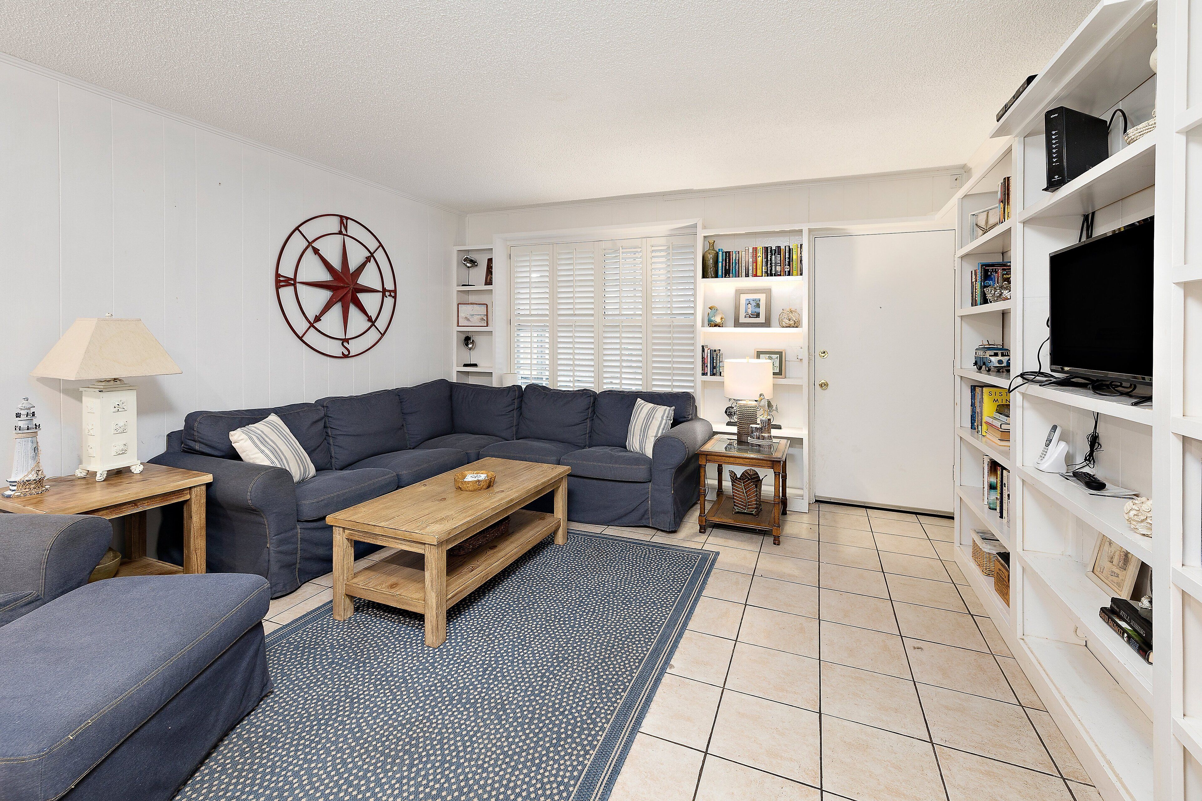A living room with a sectional sofa, a coffee table, a bookshelf, and a TV.