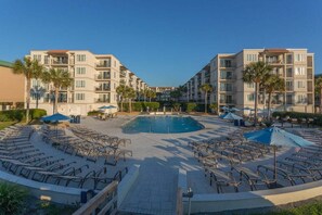 A hotel with a central pool, multiple balconies, and outdoor seating areas. - Spacious and Beachfront Condominium (Saint Simons Island)