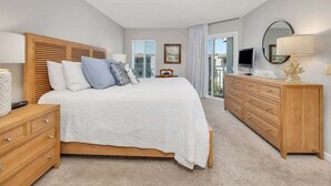 A bedroom with a bed, wooden headboard, bedside tables, a dresser, a TV, and a balcony with curtains. - Spacious and Beachfront Condominium (Saint Simons Island)