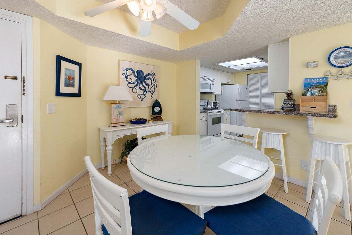 A dining area with a round glass table, white chairs, and a ceiling fan.